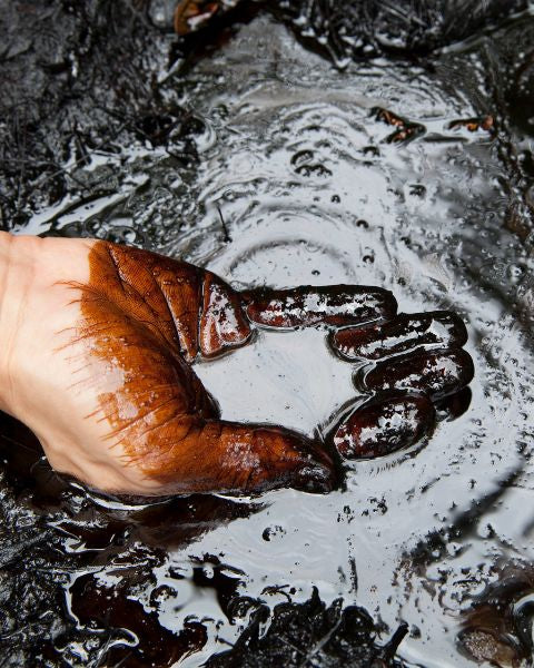 Eine Hand greift in Erdöl und hält eine kleine Menge davon in der Handkuhle